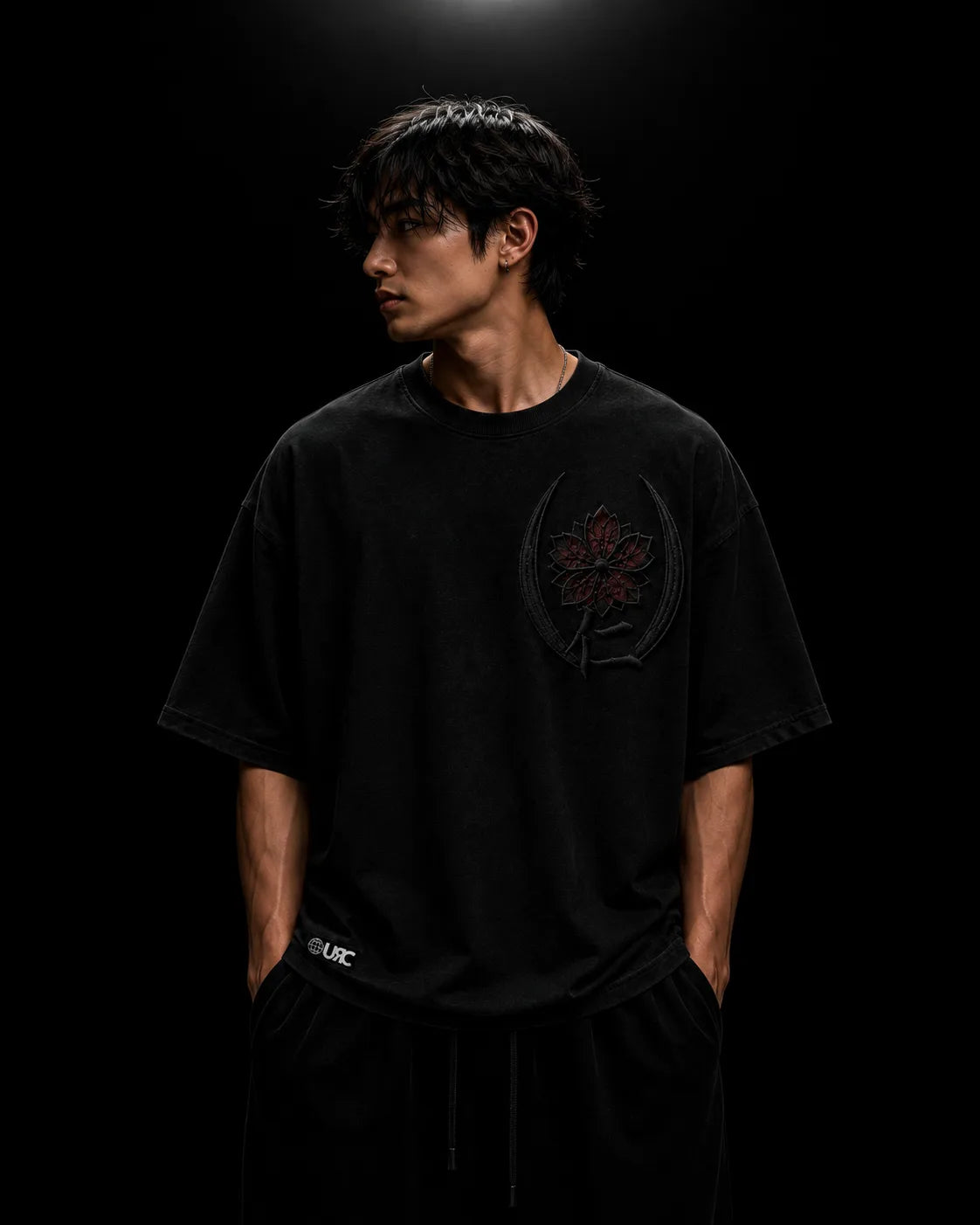 Solitary figure wearing the oversized black JIN artifact, emphasizing the engineered drop-shoulder silhouette and the ceremonial satin embroidery that rests over the heart.
