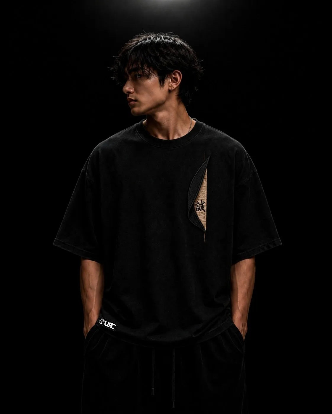 Solitary figure wearing the oversized black MAKOTO artifact, showcasing the engineered drop-shoulder architecture and sculptural raised satin embroidery.